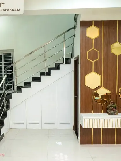 An elegant entry panel unit by the staircase in the Sithalapakkam villa, featuring wood paneling with hexagonal mirror accents and under-stair storage.