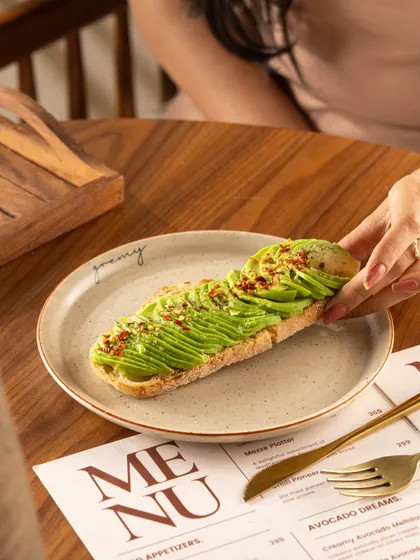 Sliced avocado toast, showing the vibrant green of the avocado. The hand reaching for a slice makes it feel interactive.