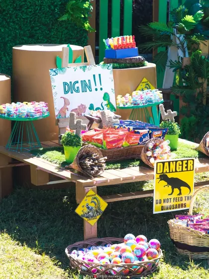 The fully stocked candy table at the dinosaur party, complete with themed signs like 'DANGER: Do not feed the dinosaurs'.