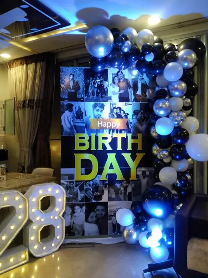 A surprise birthday party at home, made extra special with a personalized photo collage backdrop, a balloon garland, and light-up marquee numbers for the age.