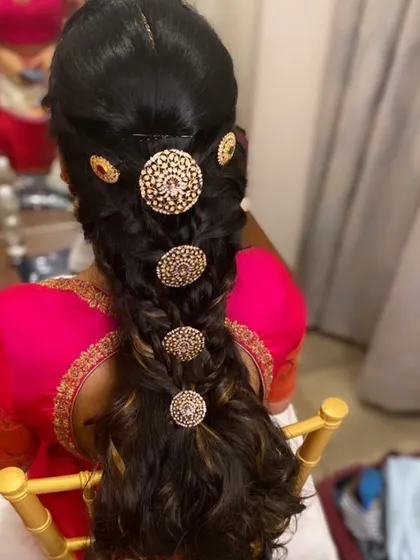 A textured, messy braid adorned with large, traditional circular gold ornaments. This style blends a modern, relaxed braid with classic South Indian jewelry.
