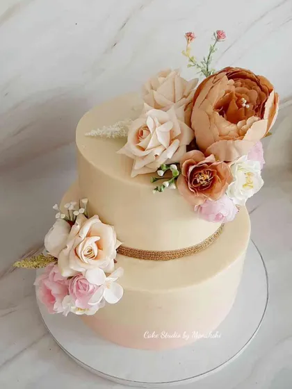 This stunning two-tier wedding cake in nude and pink shades is a true masterpiece. Finished in white chocolate ganache with no fondant, it's adorned with beautiful handcrafted sugar flowers.