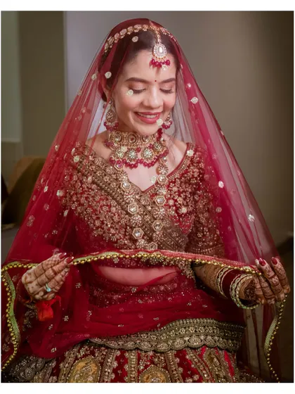 A classic bridal portrait. The bride, in her stunning red lehenga, holds her veil and smiles, the picture of happiness and anticipation.