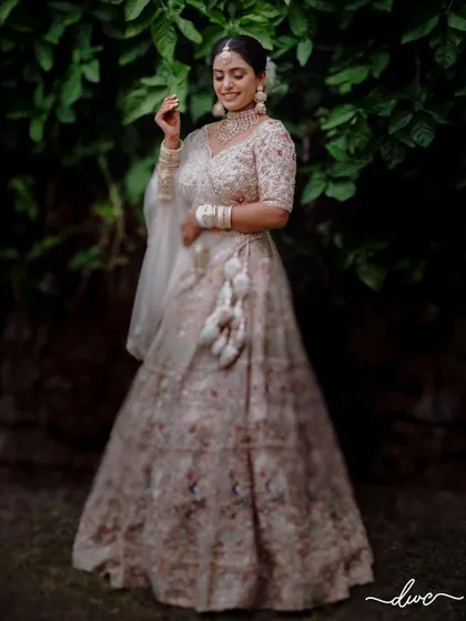 A graceful portrait of the bride in her lovely pastel lehenga, standing in a garden, her gentle smile radiating happiness.