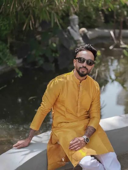 A cool portrait of the groom in sunglasses, sitting by the water during his Haldi ceremony.