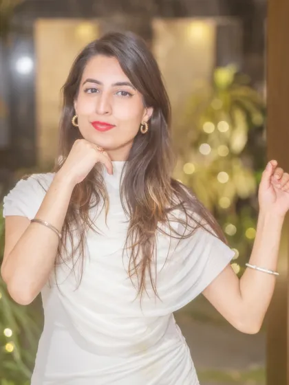 I'm posing beside the doorway with one hand raised, in a closer portrait with my white dress against the warm background.