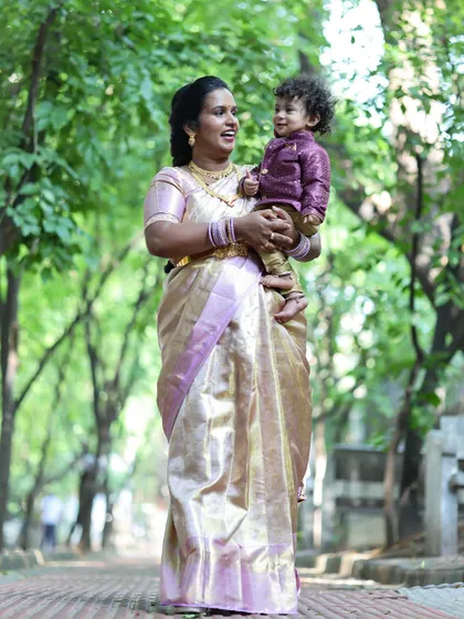 A mother and her toddler share a happy moment during an outdoor photoshoot. The natural green background adds a fresh and lively feel to the portrait.