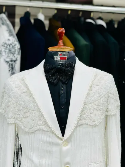 A unique white tuxedo jacket with a heavily beaded and fringed shoulder detail, paired with a black shirt and bow tie. A true showstopper for a fashion-forward client.