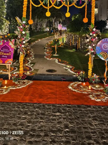 The main entrance for a Diwali party, featuring a floral arch, red carpet, and a walkway decorated with extensive flower rangoli.