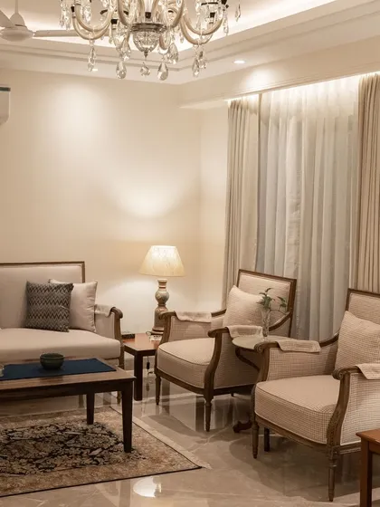 This living room setup is a study in comfy, classic design. We paired neutral-toned sofas and armchairs with dark wood tables and a traditional rug, all under the warm glow of a crystal chandelier, to create a timeless and welcoming space.