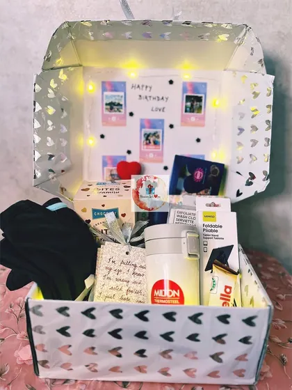 An exciting birthday box for him, lit with fairy lights and featuring a collage of polaroid photos. The box is filled with a Milton flask, a phone tripod, and other cool gadgets and treats.