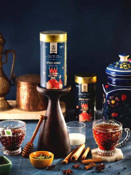 A sophisticated composition for Hindraj's Spiced Nawab Masala Tea. The product is styled with various spices like cinnamon and star anise, visually representing its rich and aromatic flavor profile.