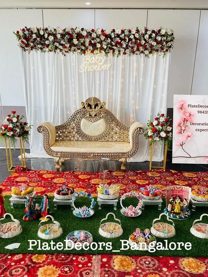A complete baby shower stage decoration with a white and red floral theme. I arranged all the seer platters, including doll-themed and fruit baskets, to create a cohesive and festive look.