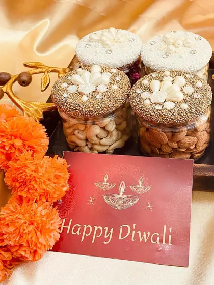 Our decorative dry fruit jars are a festive favorite. This set features four jars with intricately designed lids, filled with premium cashews and almonds, presented on a wooden tray.