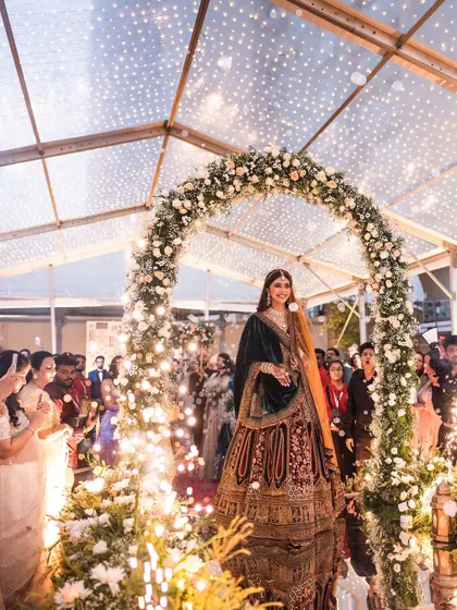 The bride's grand entrance through a floral archway, with the clear-top tent creating a magical, starry effect above.