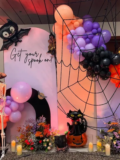 "Get your spook on!" A fun and festive Halloween party backdrop. The setup includes a giant spiderweb, a friendly skeleton, and a cascade of orange, purple, and black balloons.