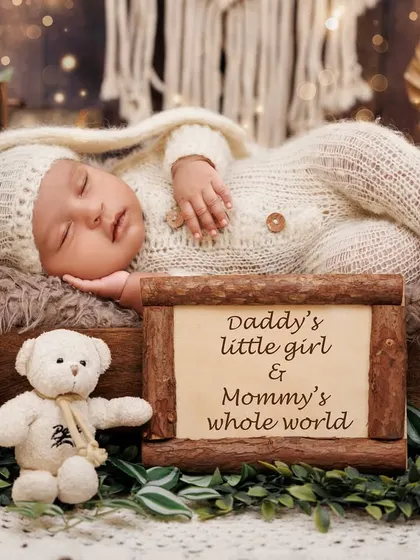 "Daddy's little girl & Mommy's whole world." A newborn sleeps peacefully in a rustic bed setup with a sweet, personalized sign.
