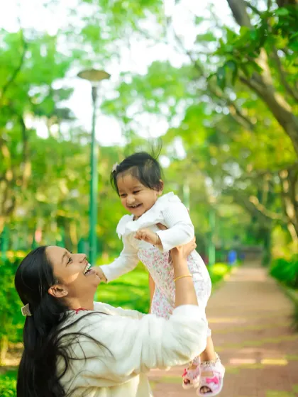 A joyful mother lifts her laughing baby girl into the air during a sunny day at the park. These are the spontaneous, happy moments we love to capture in our outdoor lifestyle photography sessions.