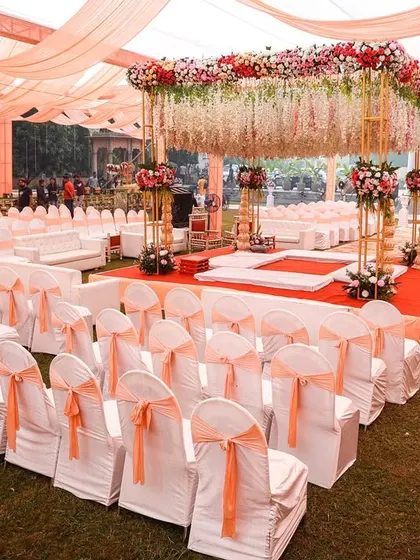 A wide view of an elegant wedding mandap with peach and white drapes and floral decor, creating a classic and sophisticated look for an outdoor ceremony.