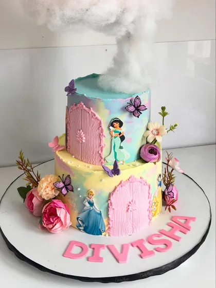 The bottom tier of the princess castle cake, featuring beloved characters like Cinderella and Jasmine, set against a pastel watercolor background with floral and butterfly accents.