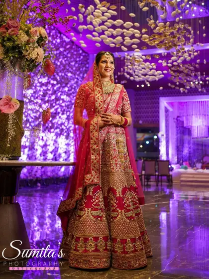 A stunning full-length portrait of the bride against a backdrop of dramatic purple lighting and floral decor. She looks absolutely regal and poised.