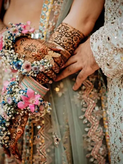 A close-up of the bride's hands, showing her intricate Mehendi design and beautiful floral jewelry (haath phool), a key detail of the bridal look.