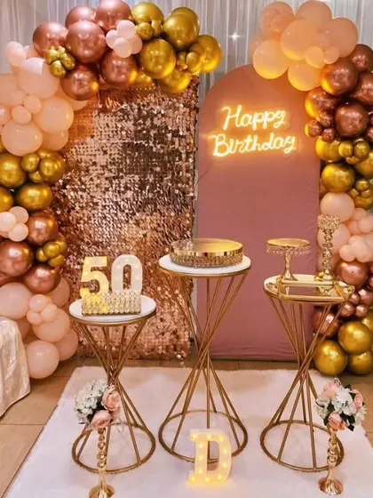 A glamorous 50th birthday celebration with a rose gold and gold theme. The decor features a sequin backdrop, a neon 'Happy Birthday' sign, and elegant balloon arches, creating a sophisticated and celebratory atmosphere for this milestone event.