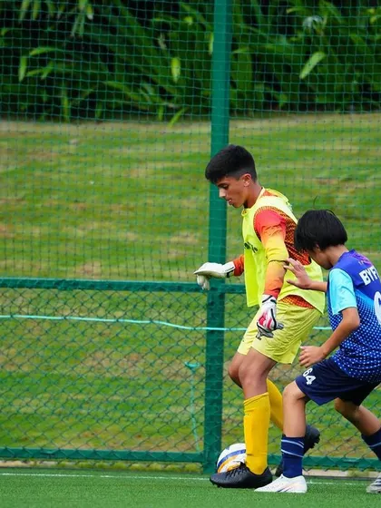 A goalkeeper works on his footwork and ball control under pressure from a teammate.