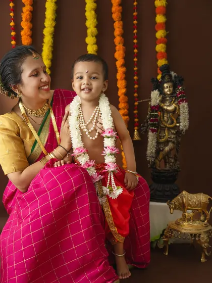 A joyful portrait of a mother and her little Krishna against a backdrop of marigold garlands.