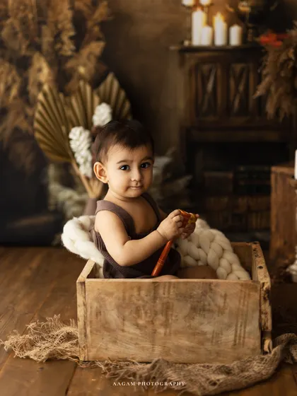 A sweet moment of a little boy playing in a wooden crate during his first birthday photoshoot. The warm, rustic setup is perfect for a cake smash or milestone session.