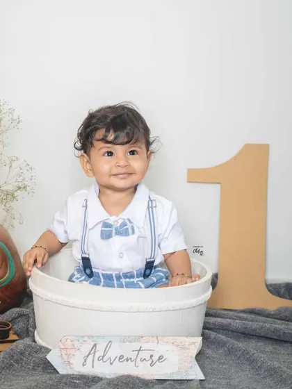 A proud one-year-old boy in his adventure-themed photoshoot. Sitting in a bucket with a large number '1' prop, he is ready to celebrate his big milestone.