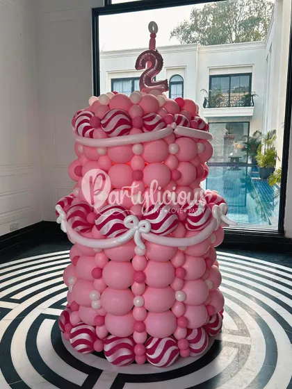 You can't have a birthday party without a cake! This two-tiered birthday cake sculpture, complete with candy-striped details and a number '2' candle, is a fun and calorie-free centerpiece.