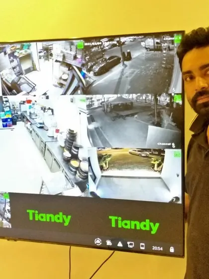 Here I am next to a large TV screen showing a multi-view display from a restaurant's Tiandy camera system. This helps the owner monitor the kitchen and dining areas.