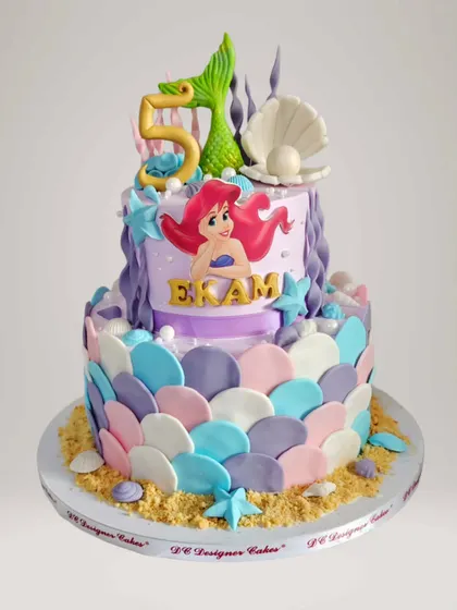 An enchanting Little Mermaid cake for a 5th birthday. This two-tier whipped cream cake features mermaid scales, seashells, and an Ariel topper, creating an underwater fantasy.