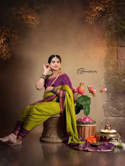 An artistic studio portrait of a mother-to-be in a traditional nauvari saree, seated with lotus flower props.
