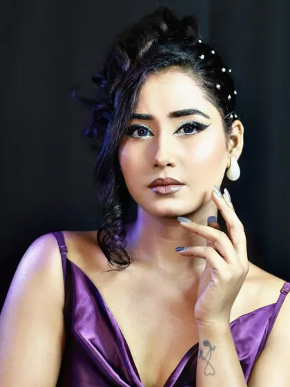 A dramatic party look with a purple satin dress and sharp winged eyeliner. The hair is styled in a messy, chic updo with pearl accents.