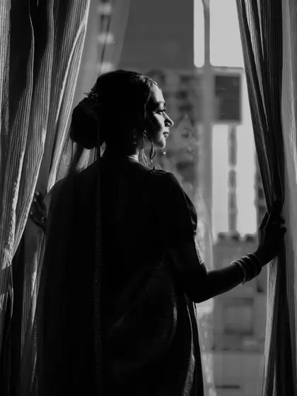 An artistic black and white silhouette of the bride looking out a window, creating a moody and timeless image.