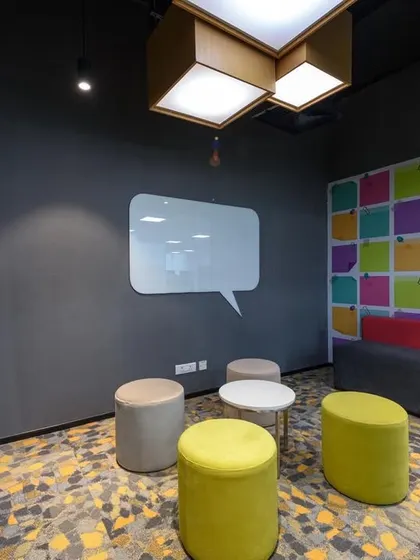 An "ideation corner" with a speech-bubble-shaped whiteboard and colorful poufs for seating. The wall features a graphic of colorful sticky notes, encouraging brainstorming.