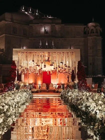 For a royal destination wedding in Jaipur, I designed this breathtaking mandap against the palace's natural architecture. The mirrored aisle reflecting the grand floral structure and ivory-and-red decor created an unforgettable, regal ambiance for the ceremony.