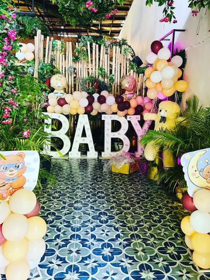 A lush, garden-style baby shower setup. The "BABY" marquee letters are surrounded by tropical plants and balloon arrangements.