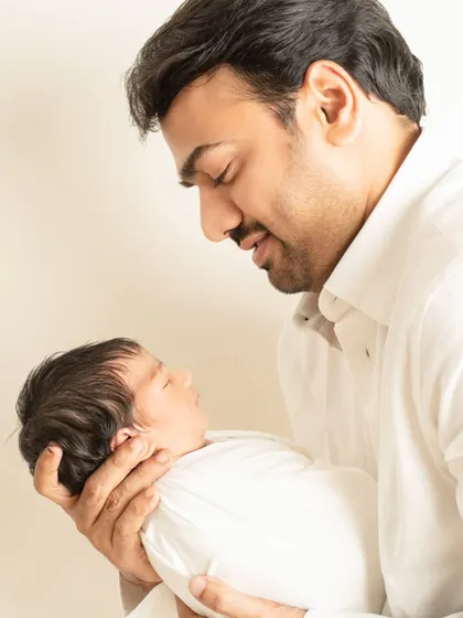 A father's gentle love is captured as he looks down at his swaddled newborn, holding the baby securely in his hands in this warm, color portrait.