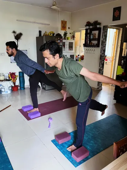 Two clients practice Virabhadrasana III (Warrior III) with blocks for support. This balancing pose builds strength in the legs and core while improving focus.