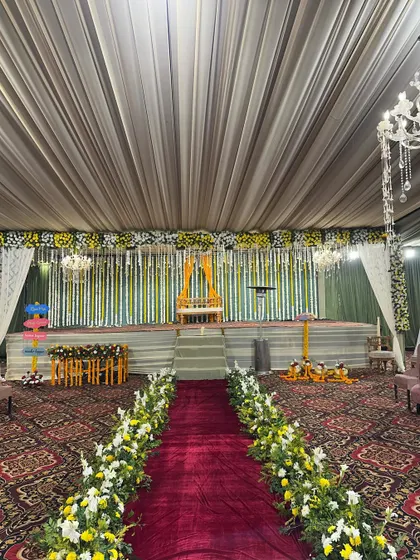 A wide view of a large Haldi setup in a banquet hall. The decor includes a decorated stage, a long floral-lined aisle, and a draped ceiling.