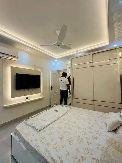 A look inside a completed bedroom at a JM Florence project. The room features a sliding wardrobe with a high-gloss finish, a simple TV unit, and a false ceiling with profile lighting.