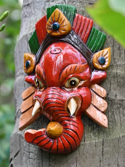 A red Ganesha mask from Nepal, mounted on a tree. Hand-carved and painted, these masks are an important part of Nepalese culture, bringing the character and emotion of the deity to life.