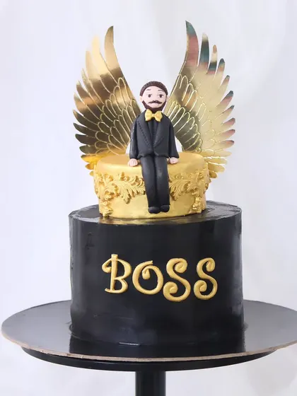 A sleek and powerful "Boss" cake. This design features a black fondant base with bold gold lettering and is topped with a custom fondant figure with impressive golden wings.