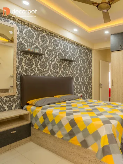 This bedroom uses a bold damask wallpaper as a feature wall behind a simple dark headboard. The yellow and grey geometric bedding adds a contemporary and cheerful touch to the room.