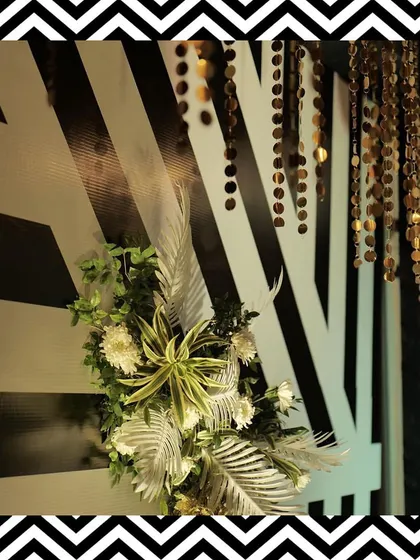 Decor details from the black and white theme, featuring golden sequin hangings and tropical leaves against a striped backdrop.