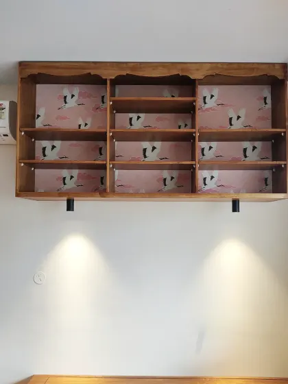 The bookcase shown empty, highlighting the beautiful crane wallpaper that serves as a backdrop. The integrated spotlights underneath illuminate the space below.