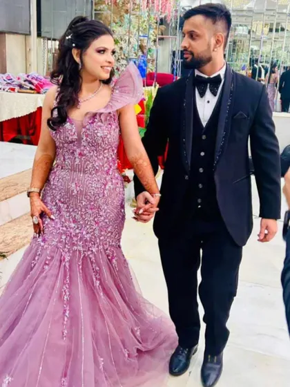 A happy couple walking hand-in-hand at their engagement. Her lavender fish-cut gown and his classic black tuxedo are a perfect match, both available for rent.